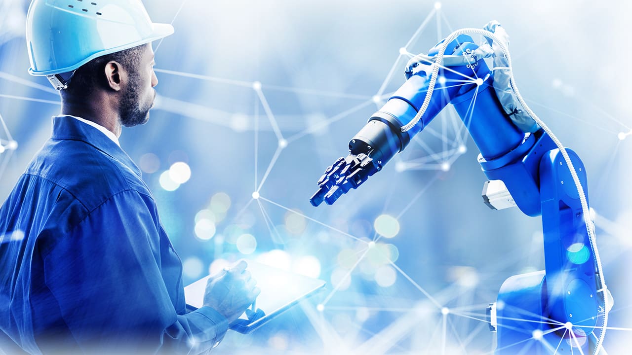 A robot arm being controlled by an industrial worker holding a tablet device.